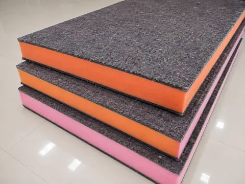 Foam mattress block with felt and foam layers visible, in a factory setting